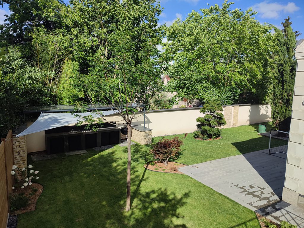 Vue d'une terrasse suspendue sur un jardin avec une cuisine d'été protégée par une verrière